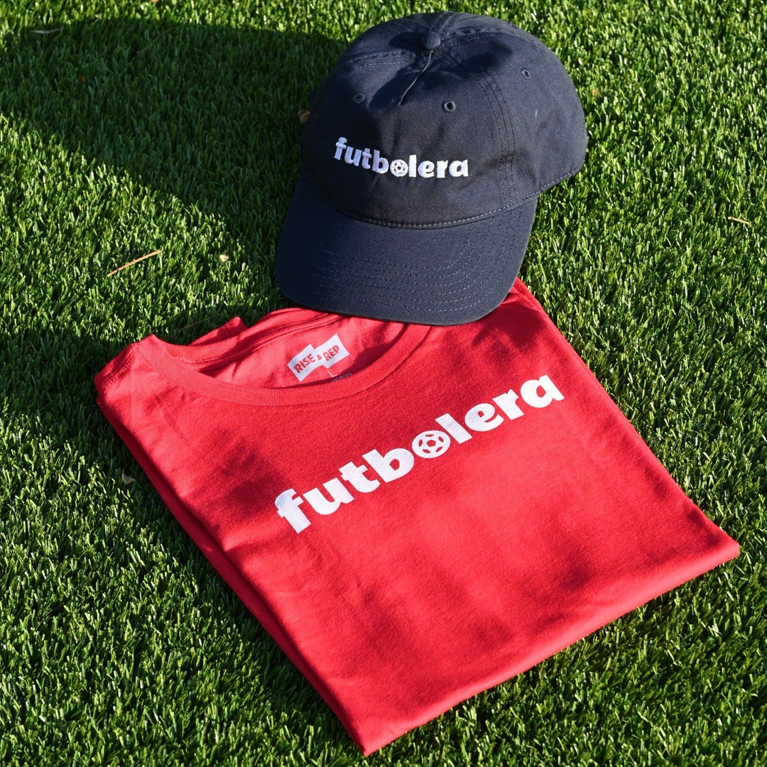 Red t-shirt and black cap with 'futbolera' branding on grass